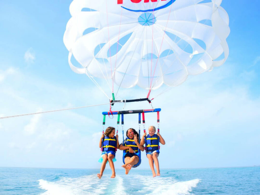 Three people parasailing over the ocean, wearing life jackets and smiling as they glide above the water.