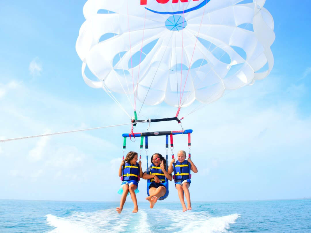 Three people parasailing over the ocean, wearing life jackets and smiling as they glide above the water.